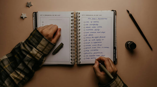A person writing down their New Year's resolutions in a notebook, with a plastic-free promise, focuses on reducing plastic consumption in 2025