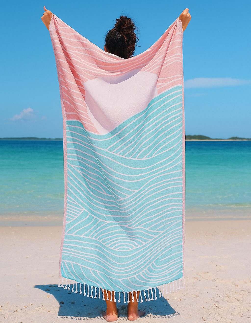 Person holding a pink and blue striped towel on a beach with clear blue water and sky.