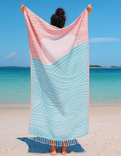 Person holding a pink and blue striped towel on a beach with clear blue water and sky.